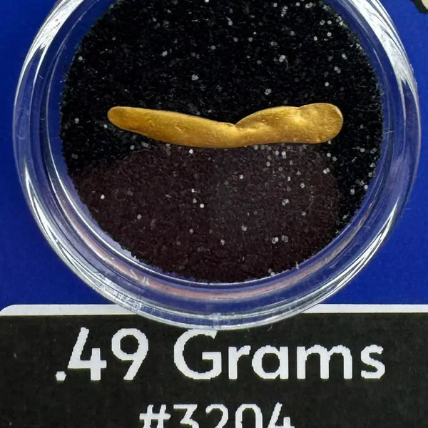 Alaska Gold nugget in a clear container with black sand, labeled '.49 Grams #3204' and 'BobbyNugget.com'.