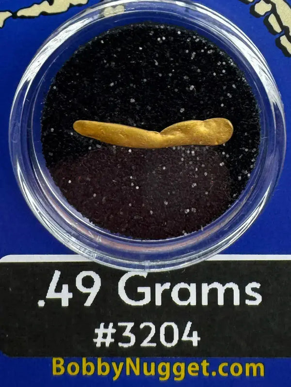 Alaska Gold nugget in a clear container with black sand, labeled '.49 Grams #3204' and 'BobbyNugget.com'.