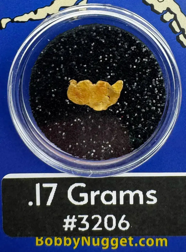 Gold nugget in a clear container with black sand on a blue background, labeled '.17 Grams #3206' and 'BobbyNugget.com'.
