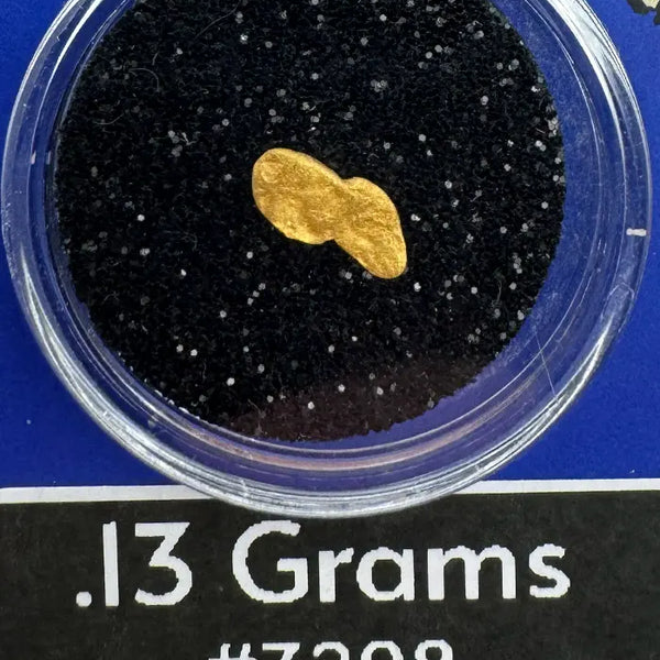 Gold nugget in a clear container with black sand, labeled '.13 Grams #3208' and 'BobbyNugget.com'.